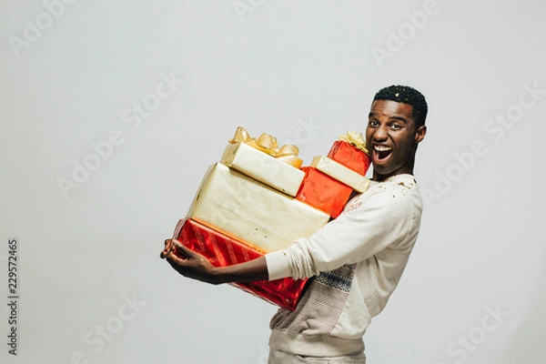 Obraz Portrait of an excited young man carrying many gifts , isolated on white studio background