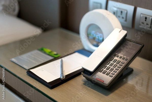 Obraz Czarny telefon i notatka z przodu i łóżko w tle, skupienie się na telefonie, obsługa pokoju, tematy komunikacji w hotelu lub ośrodku.