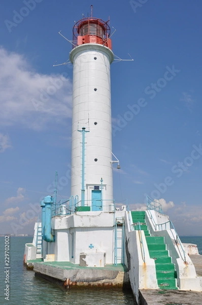 Obraz Lighthouse of Odessa port in Ukraine. Old white beacon with seascape background. Red lantern lamp on the top of lighthouse building. Green staircase to lighthouse.