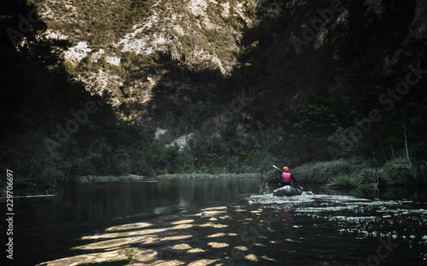 Fototapeta A lone kayaker paddling down a remote river with the sunset reflecting of the calm water