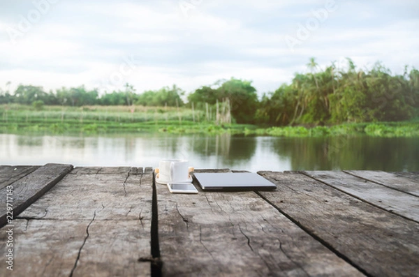 Fototapeta Coffee, bread and notebook computers placed on wooden floor in the morning of the river.Breakfast set on wooden floor in the morning.Breakfast with coffee and bread.Do not focus on objects.
