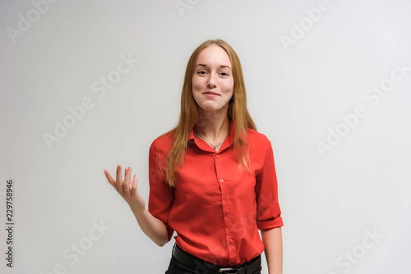 Fototapeta Studio portrait on the camera of a smiling beautiful girl with long hair talking on a white background with emotions.