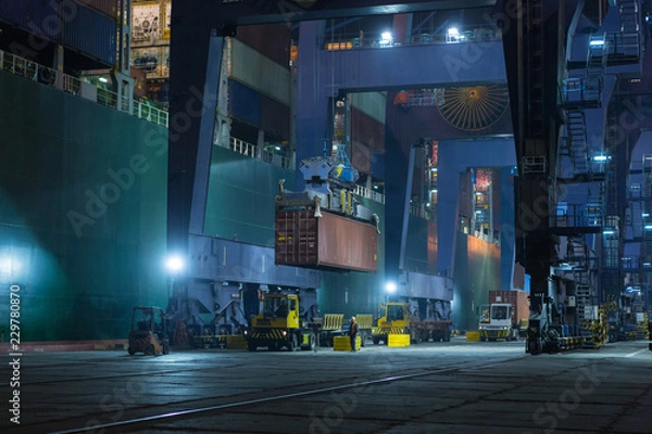 Obraz Large mooring crane unloads container ship at night. Container terminal crane will load container onto vessel. Industrial Container yard for Logistic Import Export business
