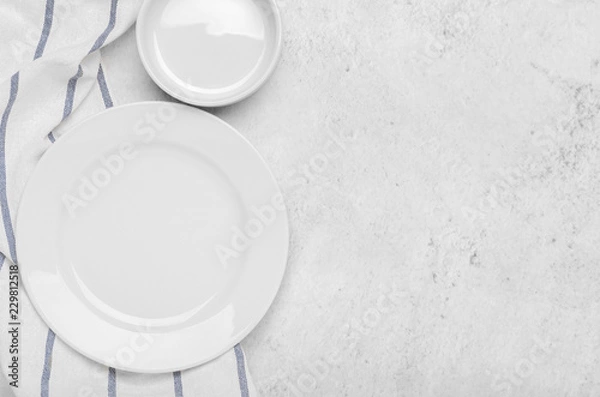 Fototapeta Clean white plates on fresh towel with stripes on a stone light minimalist background. Top view, copy space, flat lay.