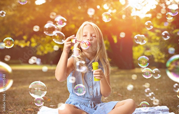 Fototapeta Portrait of a cheerful girl blowing soap bubbles