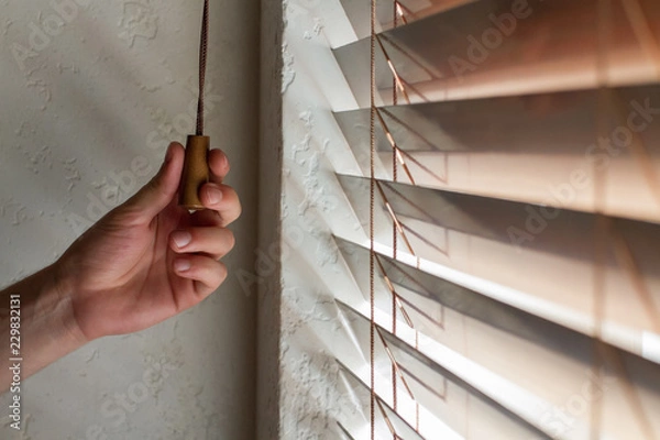Fototapeta The man's left hand holds one of the control strings of the wooden shutters on the window.