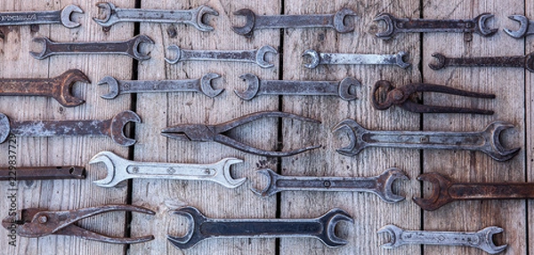 Fototapeta Metal wrench rusty tools lying on a black wooden table. Hammer, chisel, hacksaw, metal wrench. Dirty set of hand tools on a wooden panel vintage background with a tools