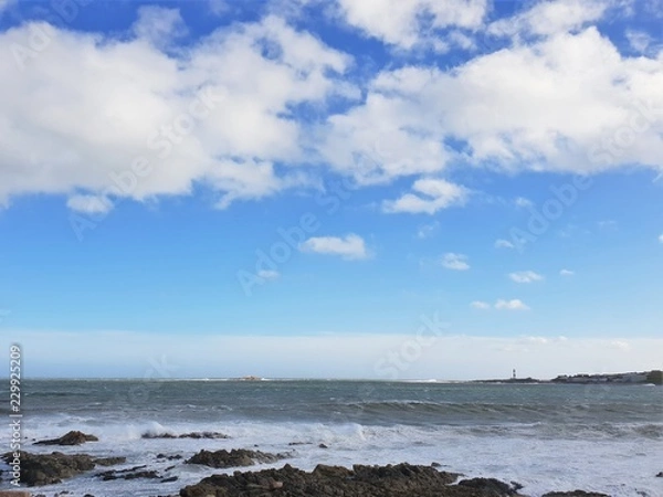 Fototapeta Fluffy white clouds in blue sky over sea with lighthouse in background
