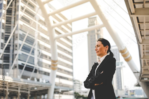 Fototapeta Portrait of a successful businesswoman standing in the middle of the city with a tall building in the background.