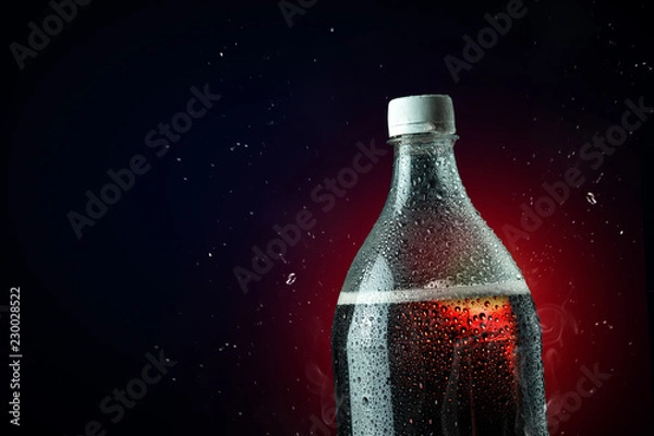 Fototapeta Cola bottle with ice splash on dark background. Soft drink bottle in celebration party concept.