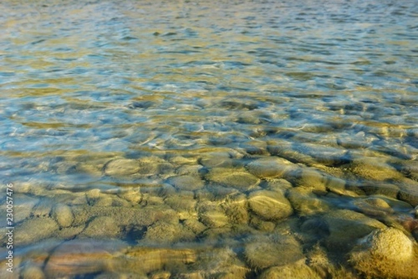 Fototapeta Pebbles under water in the rays of the sun, a mountain river, background