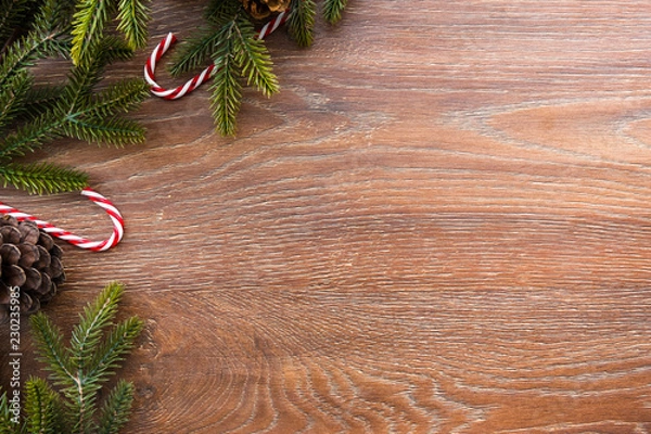 Fototapeta Christmas composition background on wood table with pine branches with cones and candy canes. Top view with copy space, flat lay.