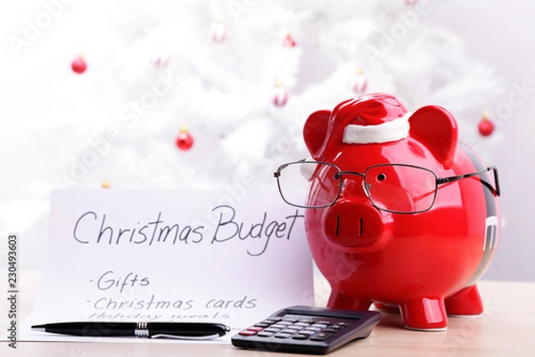 Fototapeta Skarbonka w okularach i czapce Mikołaja ze świątecznym planem budżetowym