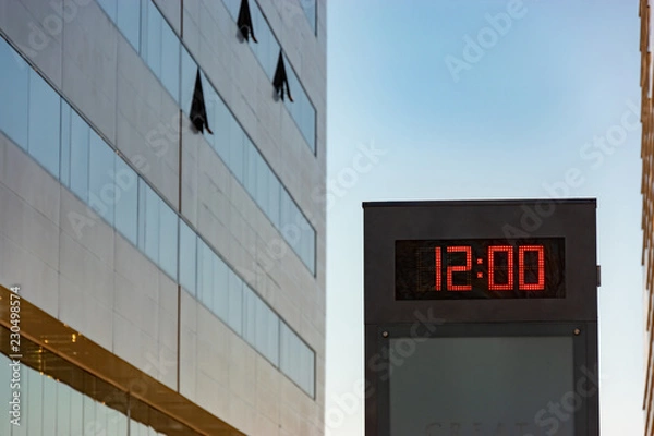 Obraz electronic display with a clock between buildings