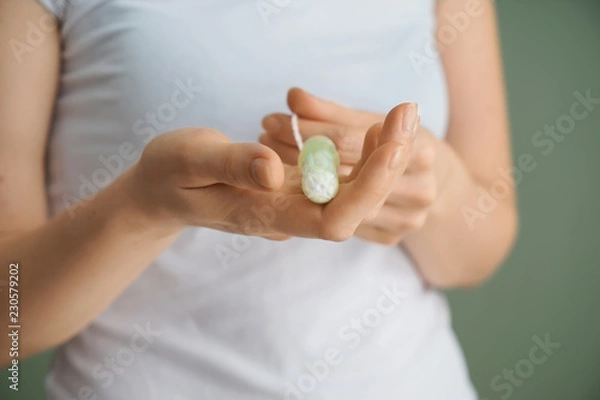 Fototapeta Woman holding tampon on color background, closeup