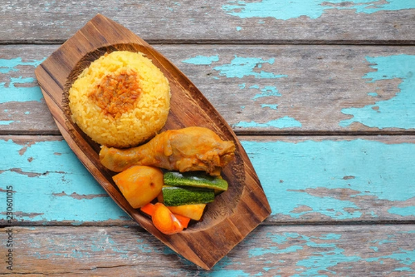 Fototapeta Top view of Malay traditional food called 'Nasi Minyak' with colorful rice, red chili ,spicy sauce, chicken, cucumber, carrot, and potato on the wooden plate.