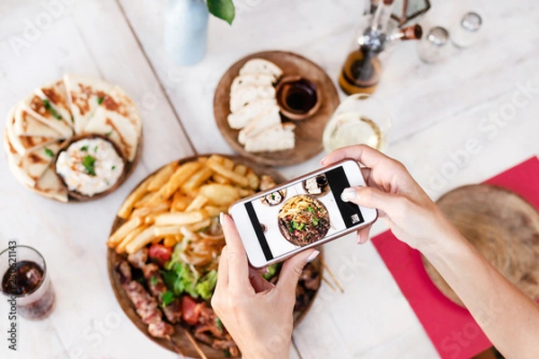 Fototapeta Kobieta robi zdjęcie danie z grilla mix przy użyciu smartfona w restauracji. Wyspa Bali. Indonezja.