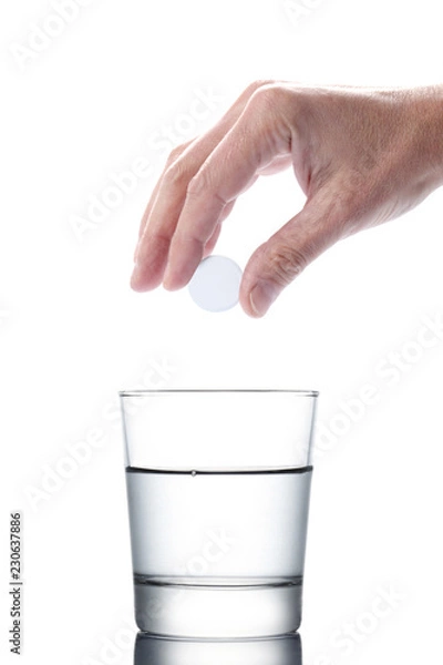 Fototapeta man's hand holding an aspirin pill dropping it in a water of glass isolated on white background with clipping path included