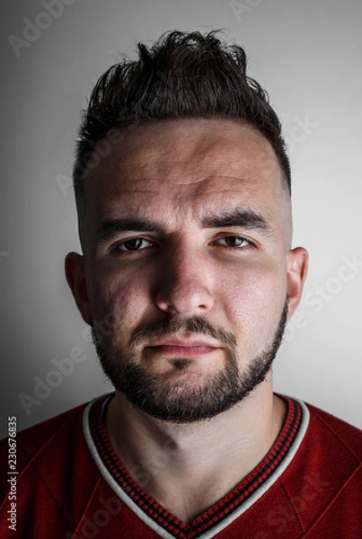 Fototapeta Close up portrait of young handsome male with beard and trendy hairdo, with serious face expression on gray background