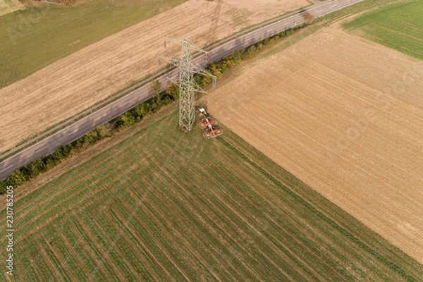 Fototapeta Bauer mit seinem Traktor bei der Grasernte am Fuße eines Strommasten