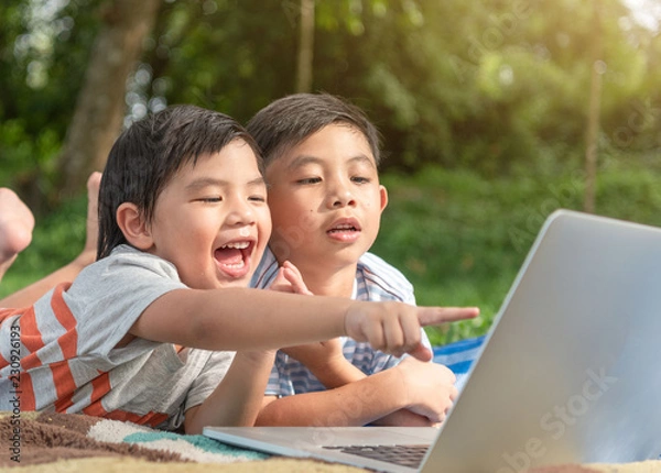 Fototapeta Little asian kids using laptop to studying . selected focus on eye with blurred background.smile kids playing laptop at garden