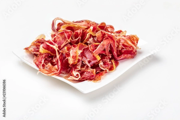Fototapeta Appetizing slices Iberian ham on a plate. Isolated on white background. Raw meat that becomes an article of haute cuisine and gastronomic luxury, through a process of raw salting and natural curing.