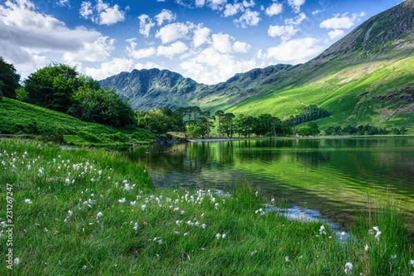 Obraz Landscape photography UK.Idyllic scenery of Lake District.Mountain lakeshore, trees  and green hills.Blue sky with few clouds above horizon.Trees and mountain reflection in water.