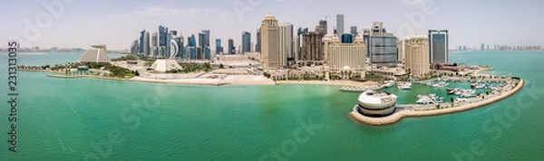Fototapeta The skyline of Doha, Qatar. Modern rich middle eastern city of skyscrapers, aerial view in good weather, midday, during hot dry summer, with view of marina and beach of Persian Gulf/Arabian Gulf