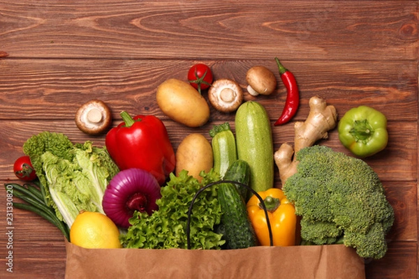 Fototapeta Fresh vegetables in a paper bag on a wooden table. Top view.
