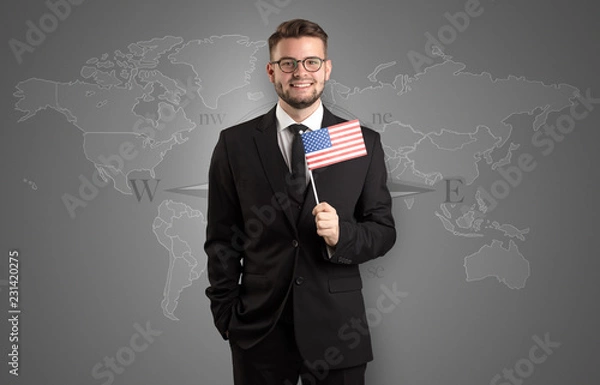 Fototapeta Cheerful businessman standing in front of a map with flag on his hand
