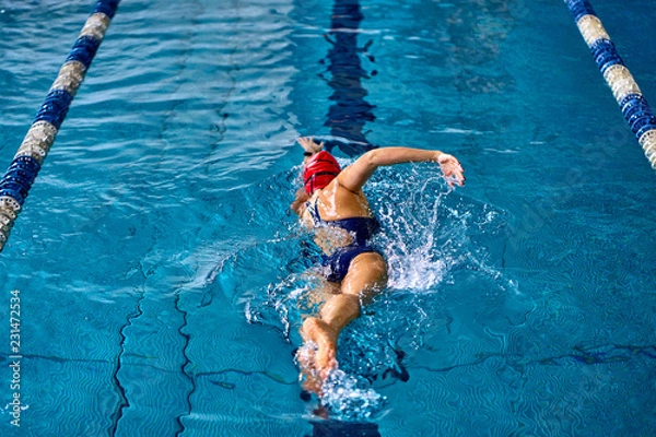 Fototapeta Female athlete swimming fast in crawl style.  Splashes of water scatter in different directions.