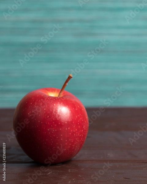 Fototapeta Isolated red mcintosh apple on wooden surface with green and blue background	