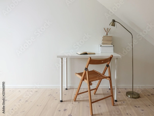 Fototapeta Simple workspace interior. Open book in minimalist home office room. Lamp, books, wooden floor and folding chair. Empty white wall and desk for copy space.