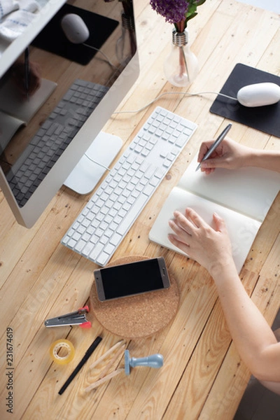 Obraz Hands of a Business woman is writing book as notepad or Take notes on Her wooden table desk  . Business Success Working at home office with notebook and computer for marketing and part time Concept.