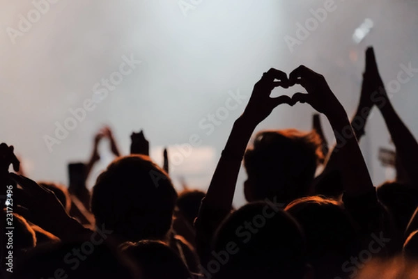 Obraz Hands silhouettes of the crowd raised up at music show. Heart made by fingers