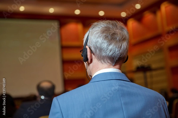 Fototapeta Unrecognizable business people using headphones for translation during event . bald security guard with the headset to control people . heated debate at a conference discussion