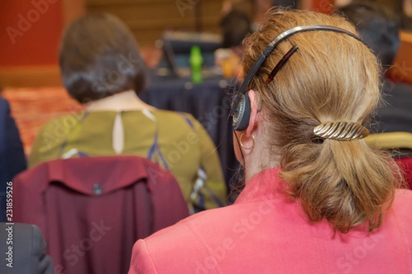 Fototapeta Unrecognizable business people using headphones for translation during event . bald security guard with the headset to control people . heated debate at a conference discussion