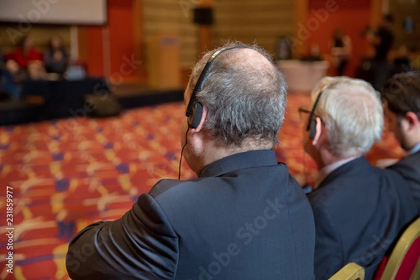 Fototapeta Unrecognizable business people using headphones for translation during event . bald security guard with the headset to control people . heated debate at a conference discussion
