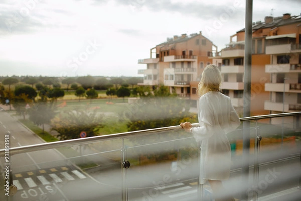 Obraz Back view of young girl dressed in bathrobe on balcony. Park outdoor background.