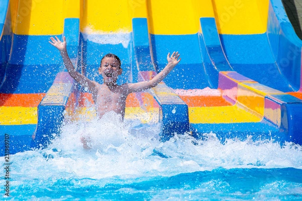 Obraz Cheerful boy splashing water on water slide at aqua park