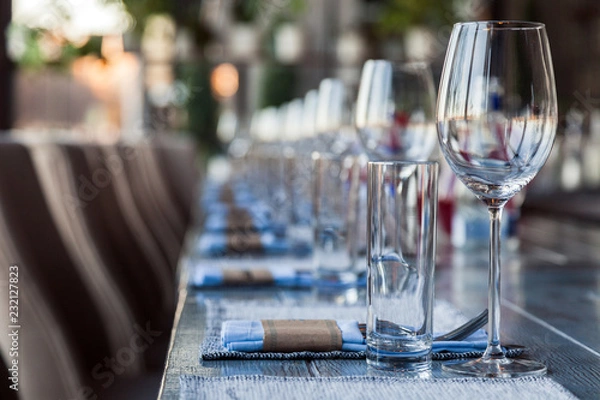 Fototapeta Restaurant serving and glass wine and water glasses, forks and knives on textile napkins stand in a row on a gray wooden table. Concept banquet, birthday, conference, group lunch