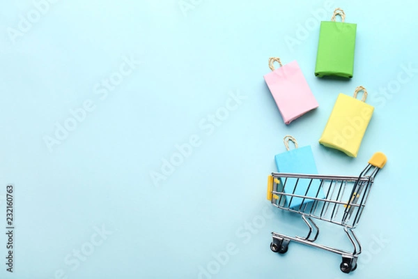 Obraz Małe papierowe torby na zakupy z koszykiem na niebieskim tle