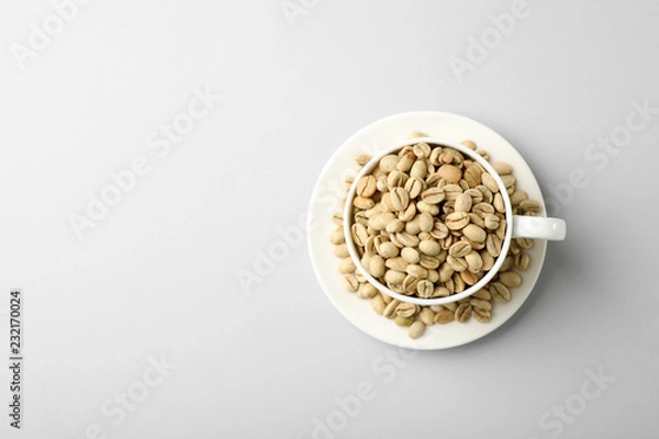 Fototapeta Cup and saucer with green coffee beans on white background, top view. Space for text