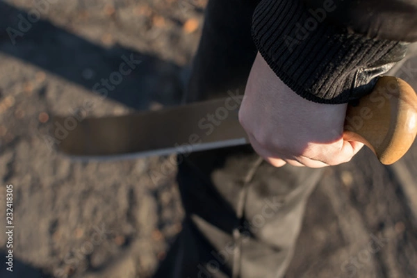 Fototapeta machete in the hand of a man on the street in black clothes