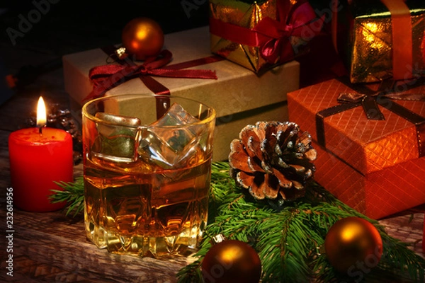 Fototapeta Glass with cognac or whiskey, Christmas balls and candles. New Year's tree, balls and glass with alcohol.