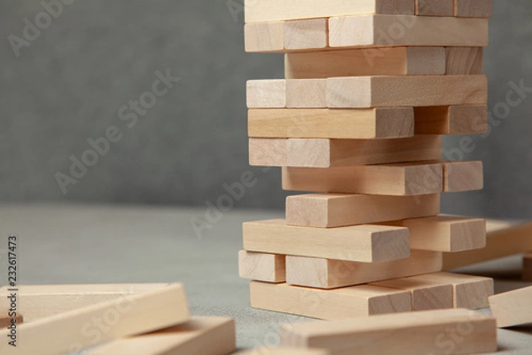 Fototapeta Tower of wooden blocks on gray background. Board game for the whole family or party. Concept of building business or building team.