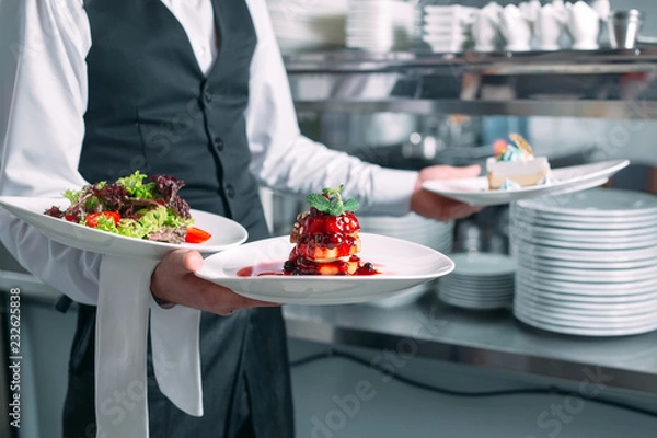 Fototapeta Waiter serving in motion on duty in restaurant. The waiter carries dishes