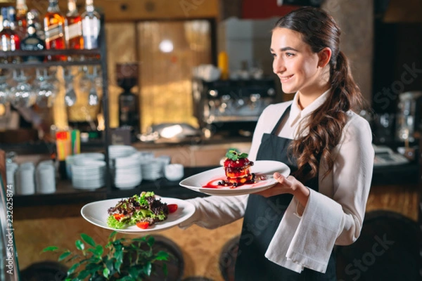 Fototapeta Waiter serving in motion on duty in restaurant. The waiter carries dishes