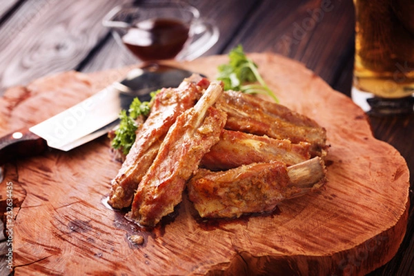 Obraz Roasted spare ribs on a wooden board with meat hatchet, BBQ sauce and glass of beer on a rustic wooden table