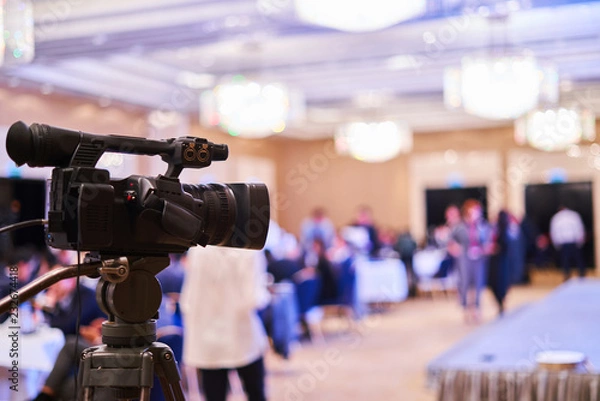 Fototapeta video camera stands on a tripod - video of the conference, blurred background